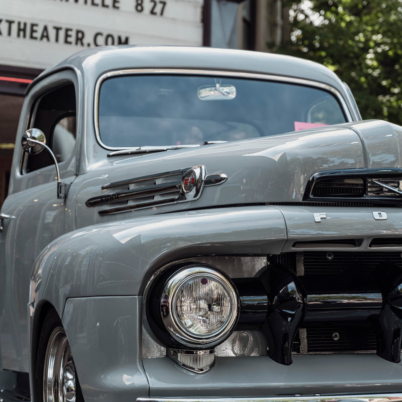 Vintage gray car with a clear focus on the front, including headlights and grille, with a blurred background.