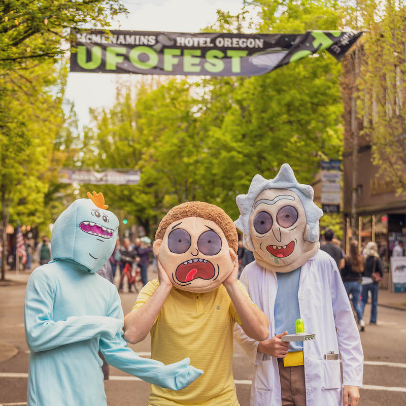 Three people in costumes at UFO Fest event with a banner in the background.